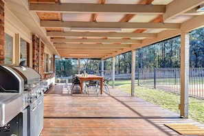 Eine überdachte Terrasse im Freien mit Grill, Esstisch und Stühlen.