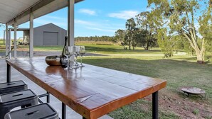 An outdoor dining area with a long wooden table, black chairs, and a bottle of wine. - The Reserve Homestead walk to vineyards (Pokolbin)