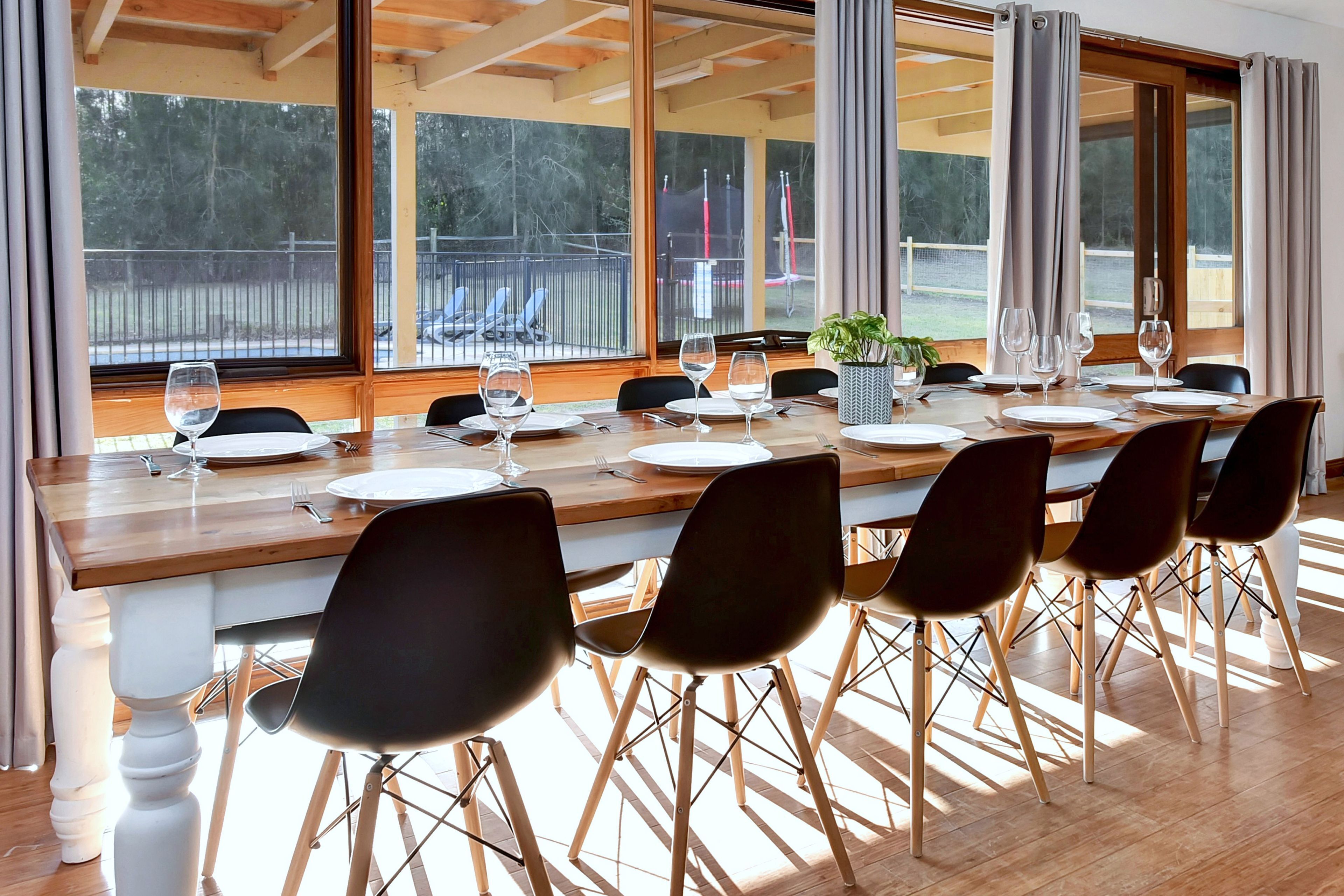A dining area with a long wooden table set for six, surrounded by black chairs with wooden legs.