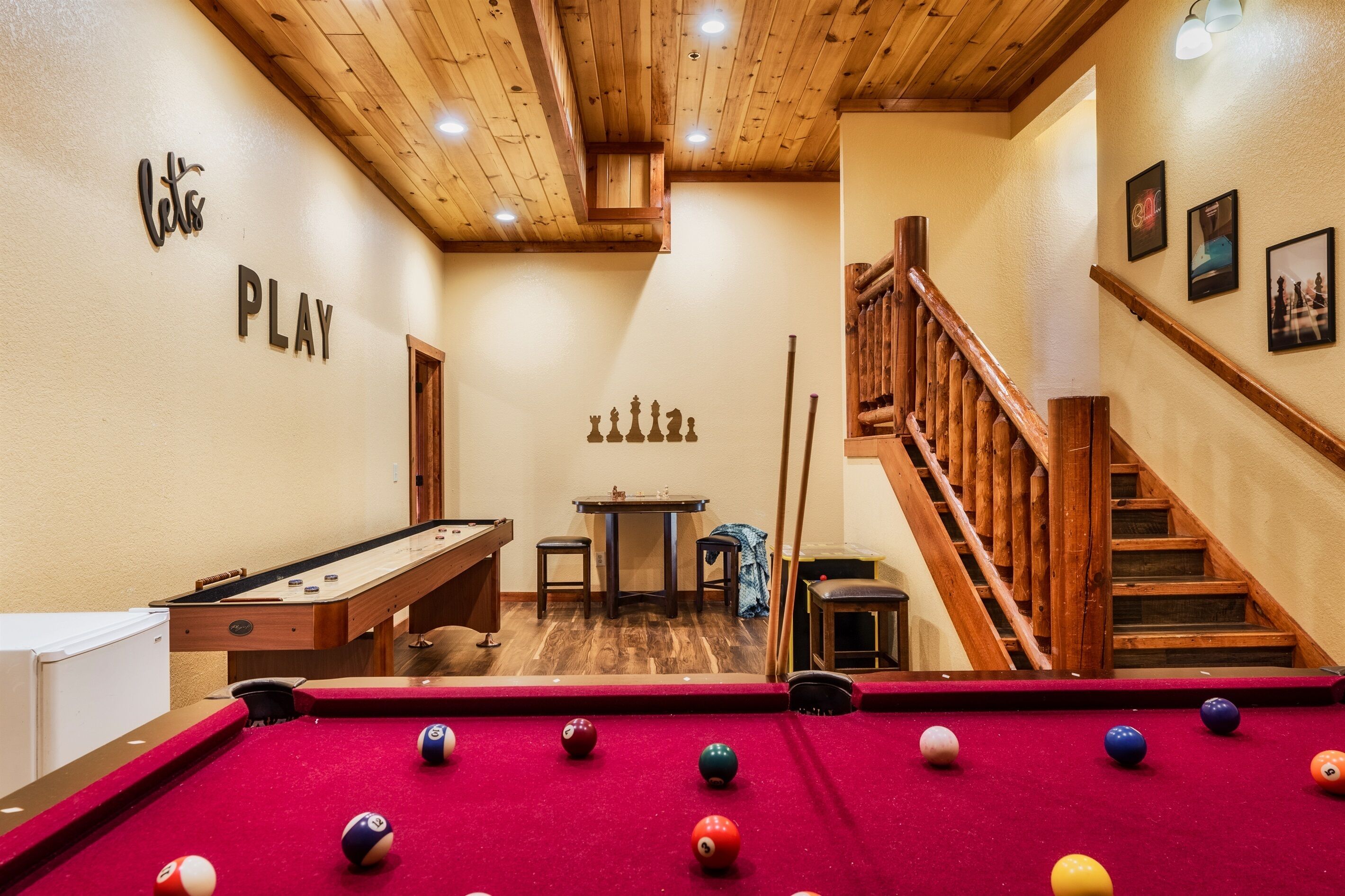 Een pooltafel met ballen, een biljartkeu en een pooltafel in een ruimte met houten vloeren en een houten trap.