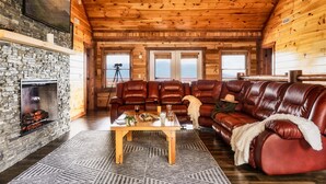 L’intérieur chaleureux d’un chalet avec une cheminée en pierre, des canapés en cuir et un plafond en bois.