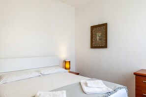 A neatly made bed with white linens, a bedside lamp, and a framed picture on the wall.