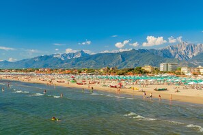 A beach with umbrellas, people, and mountains in the background.