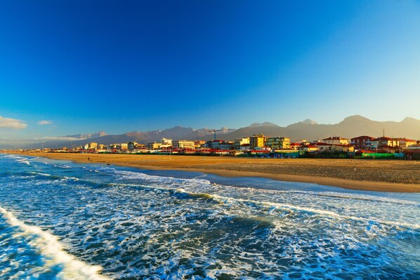 A coastal cityscape with buildings along the beach and mountains in the background.