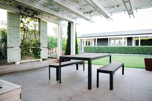 An outdoor patio with a table and benches, a covered area with a pergola, and a building in the background. - Getaway on Grey - Pool and 4 bedrooms (Martinborough)
