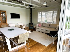 A modern living room with a white table, wicker chairs, a beige sofa, and a glass door leading outside.