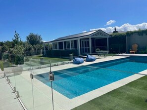 A swimming pool with a covered patio area, a chair, and a small deck.