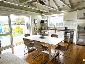 A modern kitchen with a dining area, featuring a large table, wicker chairs, and a view of the outdoors.