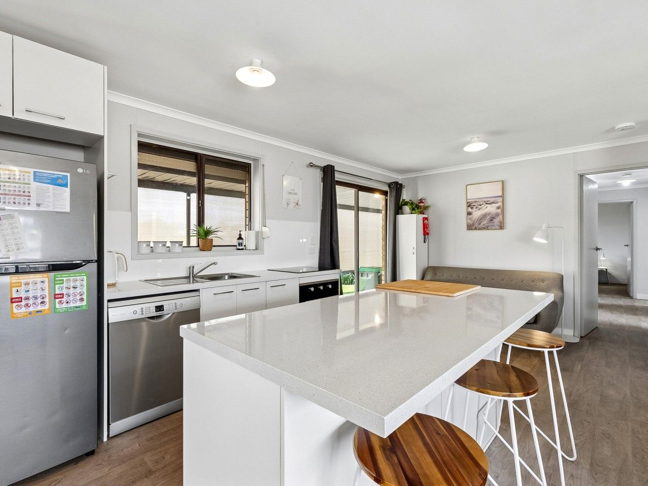 A modern kitchen with a central island, bar stools, a dishwasher, and a refrigerator.