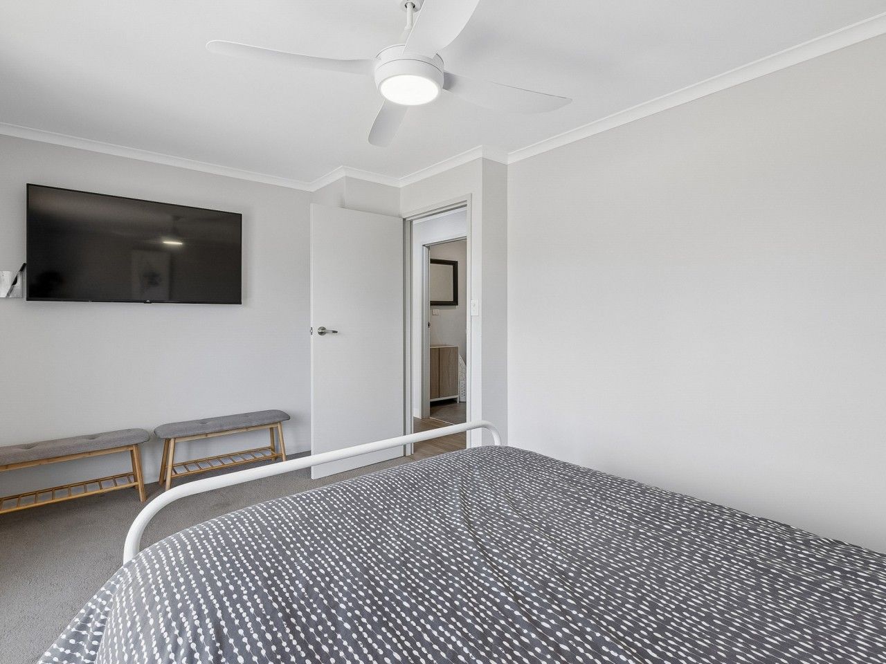Une chambre à coucher comprenant un lit, un banc, un ventilateur de plafond et un téléviseur fixé au mur.