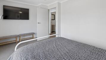 Une chambre à coucher comprenant un lit, un banc, un ventilateur de plafond et un téléviseur fixé au mur.