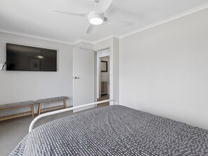 A bedroom with a bed, a bench, a ceiling fan, and a TV mounted on the wall.