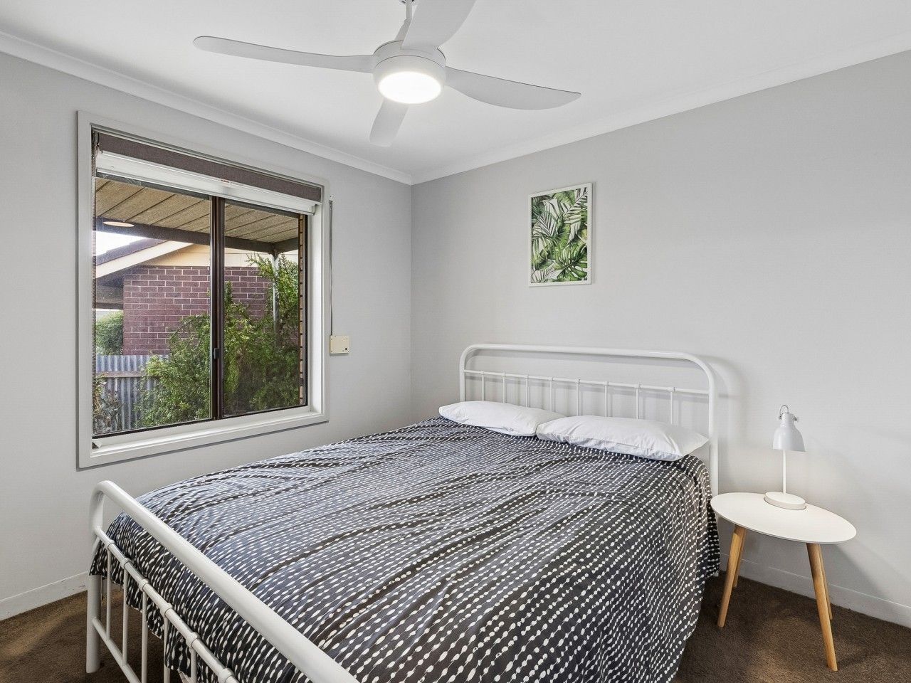 A bedroom with a bed, a ceiling fan, a window, and a bedside table.
