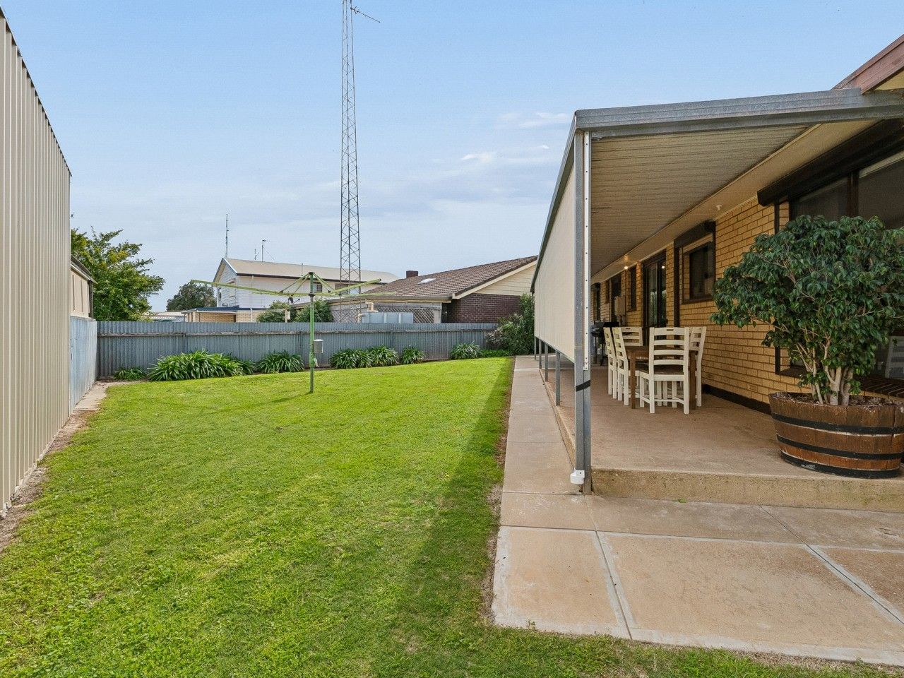 A residential backyard with a lawn, a patio area with chairs, and a tall communication tower in the background.