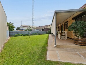 A residential backyard with a lawn, a patio area with chairs, and a tall communication tower in the background.
