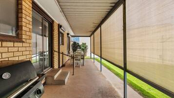A covered outdoor area with a barbecue grill, a concrete pathway, and a view of a building with a brick facade.