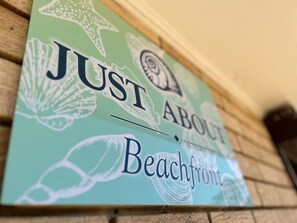 Een wandbord met de tekst 'JUST ABOUT Beachfront' en decoratieve schelpen.
