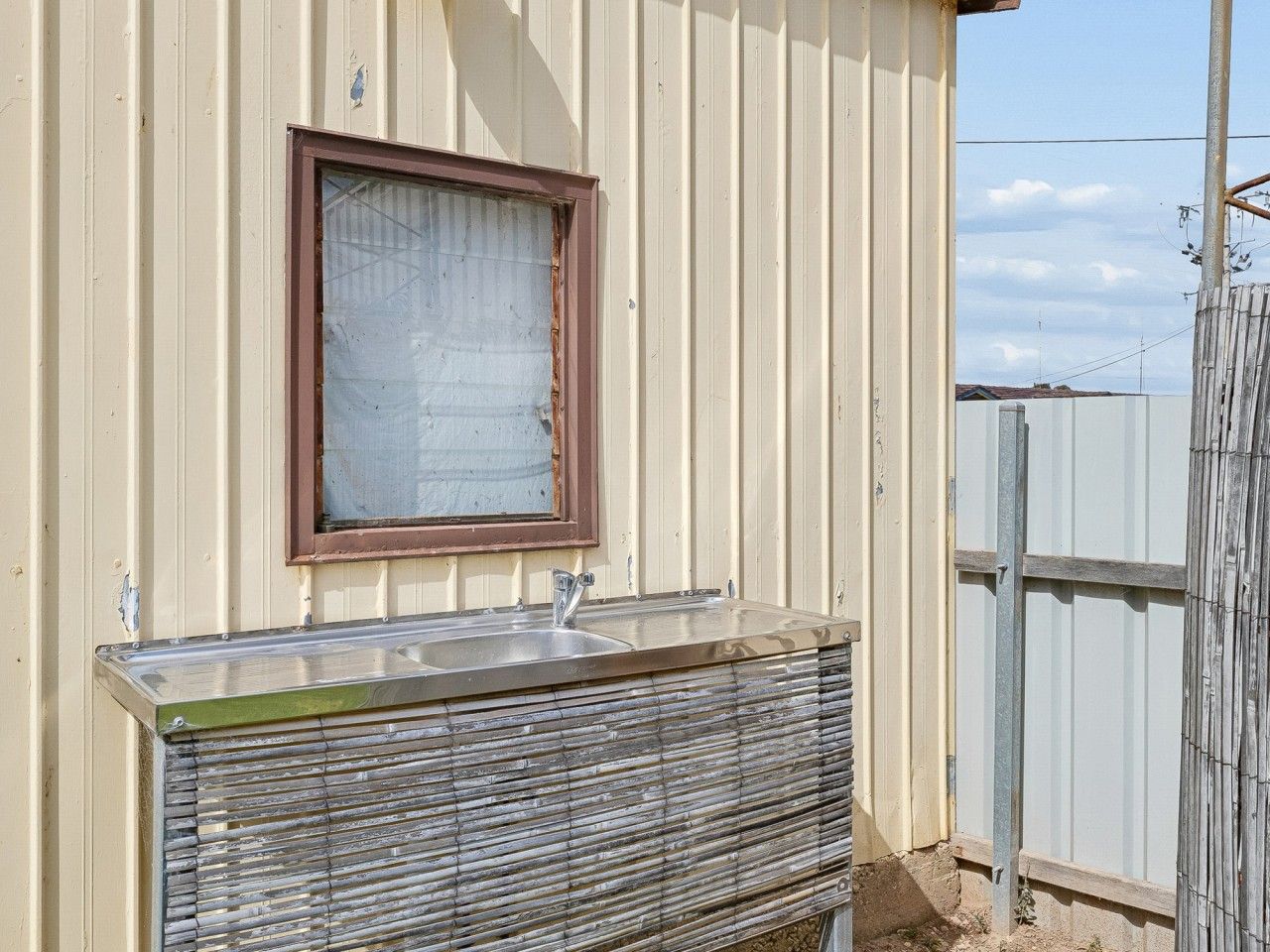 A metal-framed outdoor sink with a window above it, set against a corrugated metal wall.