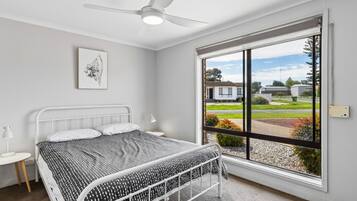 A bedroom with a bed, a ceiling fan, a window with a view of the outside, and a small bedside table.