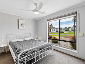 Un dormitorio con cama, ventilador de techo, ventana con vista al exterior y una mesita de noche pequeña.