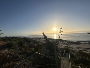 Een kustlandschap met een zonsondergang boven de oceaan, een strand en een trap die naar de kust leidt.