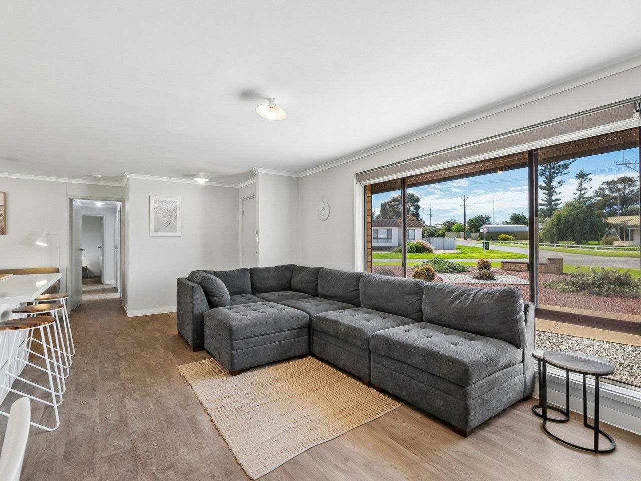 A modern living room with a sectional sofa, a dining area with bar stools, and a large window offering a view of the outdoors.