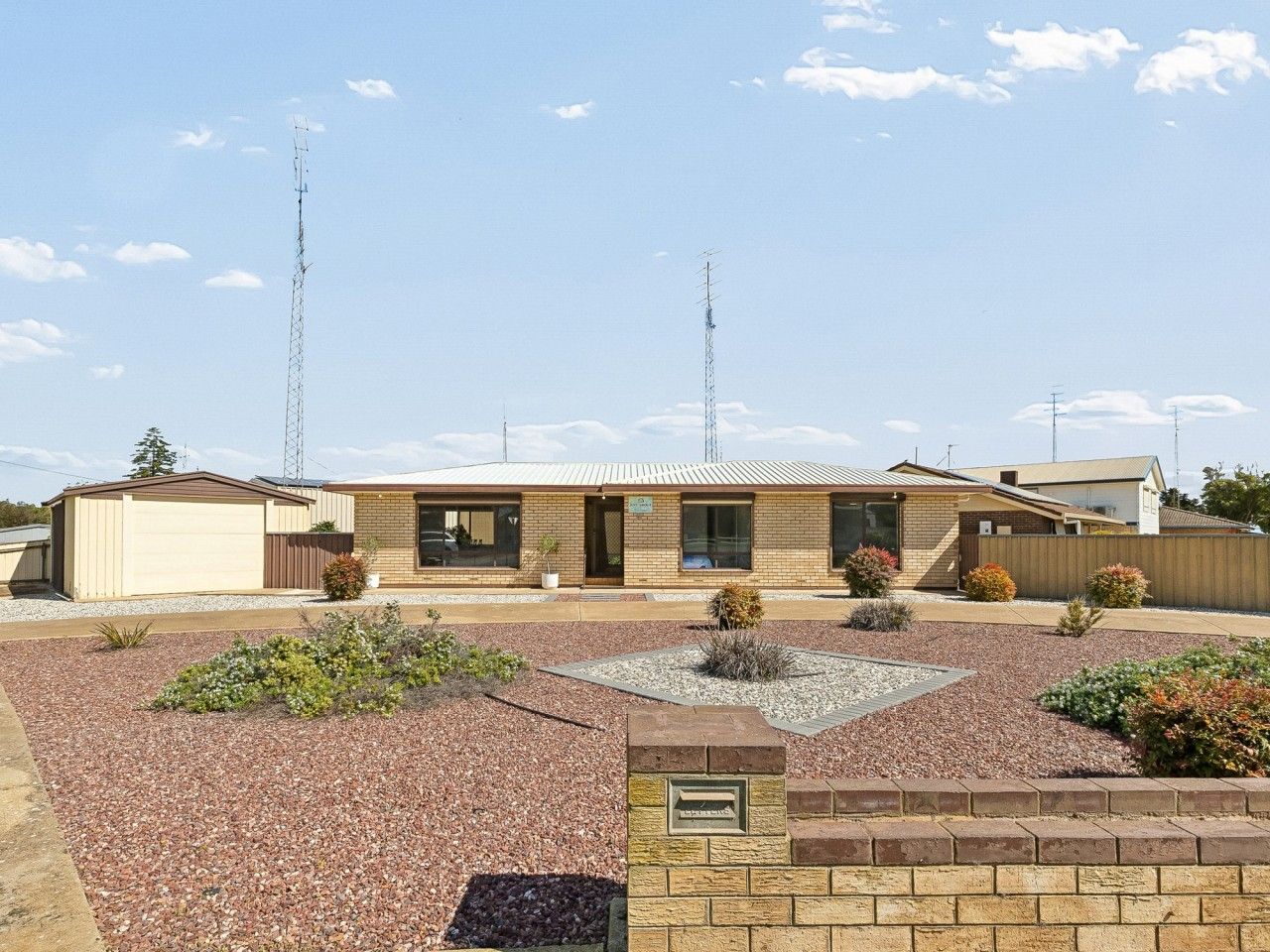 A single-story building with a brick facade, a small front garden with gravel and plants, and a clear sky.