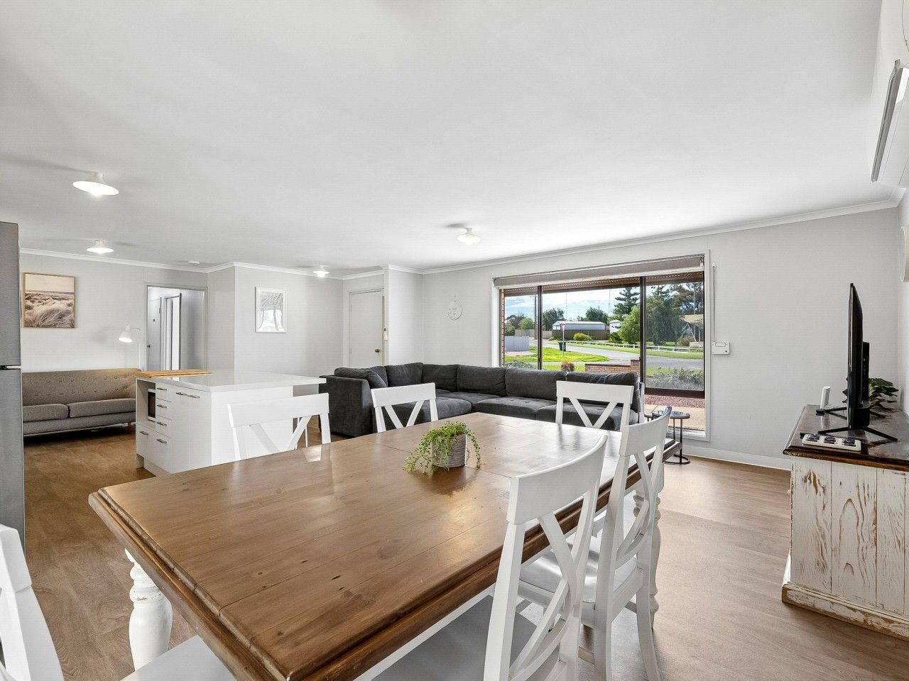 A modern kitchen with white cabinetry, a wooden dining table, and a large window offering a view of the outdoors.