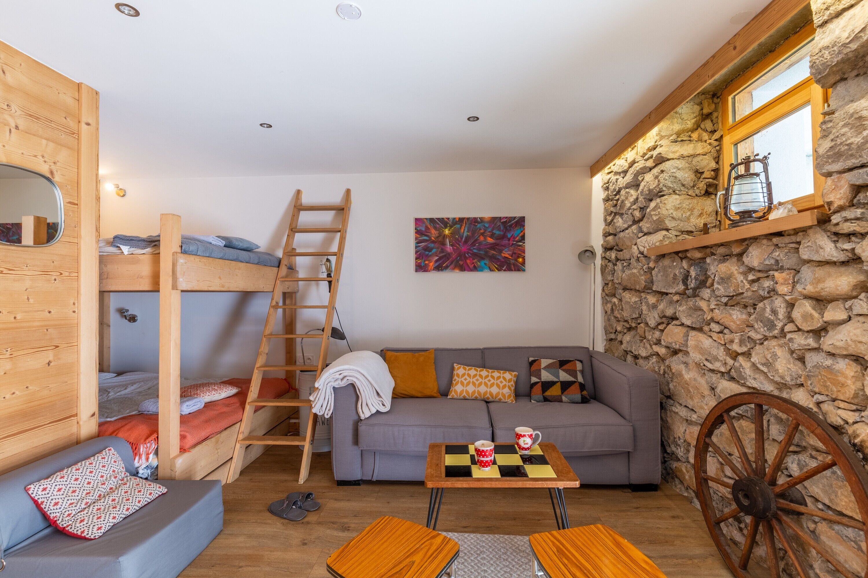 Una habitación acogedora con literas, un sofá, una mesita y una pared de piedra.