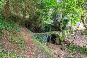 Une zone boisée avec un pont de pierre, un sentier de terre et un mur de pierres.