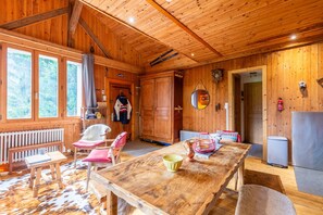 Interior de una cabaña de madera con una mesa de comedor, sillas, un banco, una chimenea y una zona de cocina.