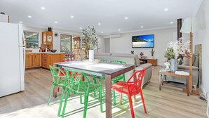 Eine moderne Küche mit Holzschränken, einem Essbereich mit Tisch und Stühlen, einer Couch und einem an der Wand montierten Fernseher.