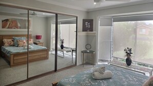 Ein Schlafzimmer mit einem großen Spiegel, einem Bett mit floralem Bettbezug, einem Deckenventilator und Blick durch eine Glastür.