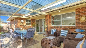 Eine überdachte Terrasse mit Backsteinwand, einem Esstisch mit Stühlen und Korbmöbeln.
