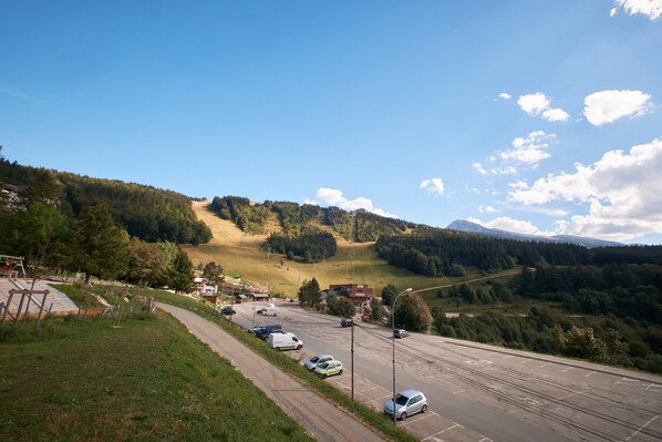 A parking lot with cars, a road, and a hilly landscape with trees and buildings in the background.