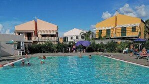 Une piscine à l’eau claire, entourée d’immeubles dotés de balcons et de parasols.