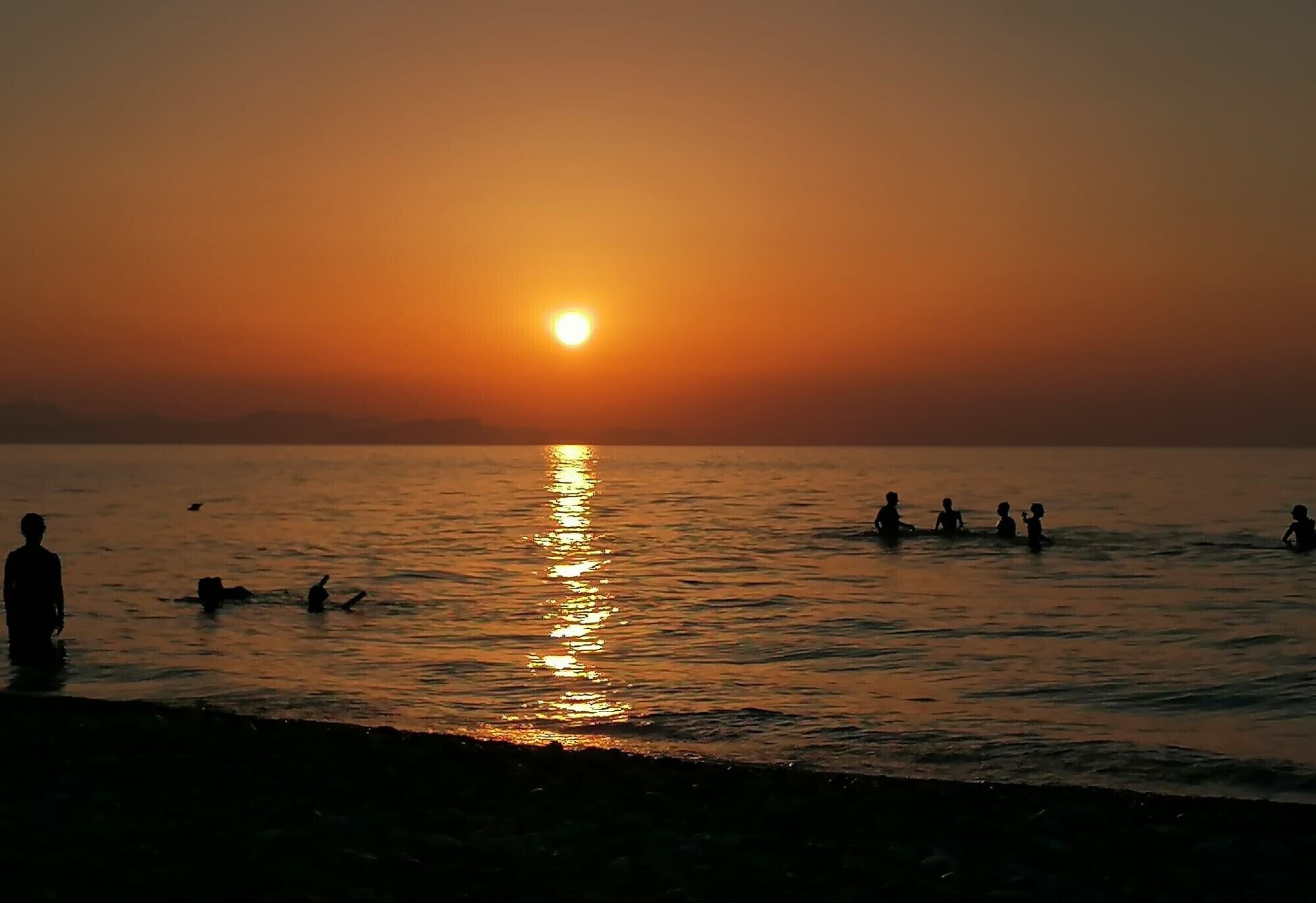 Ein Sonnenuntergang über einem Gewässer mit Silhouetten von Menschen und einem Hund.