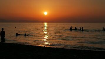 Ein Sonnenuntergang über einem Gewässer mit Silhouetten von Menschen und einem Hund.