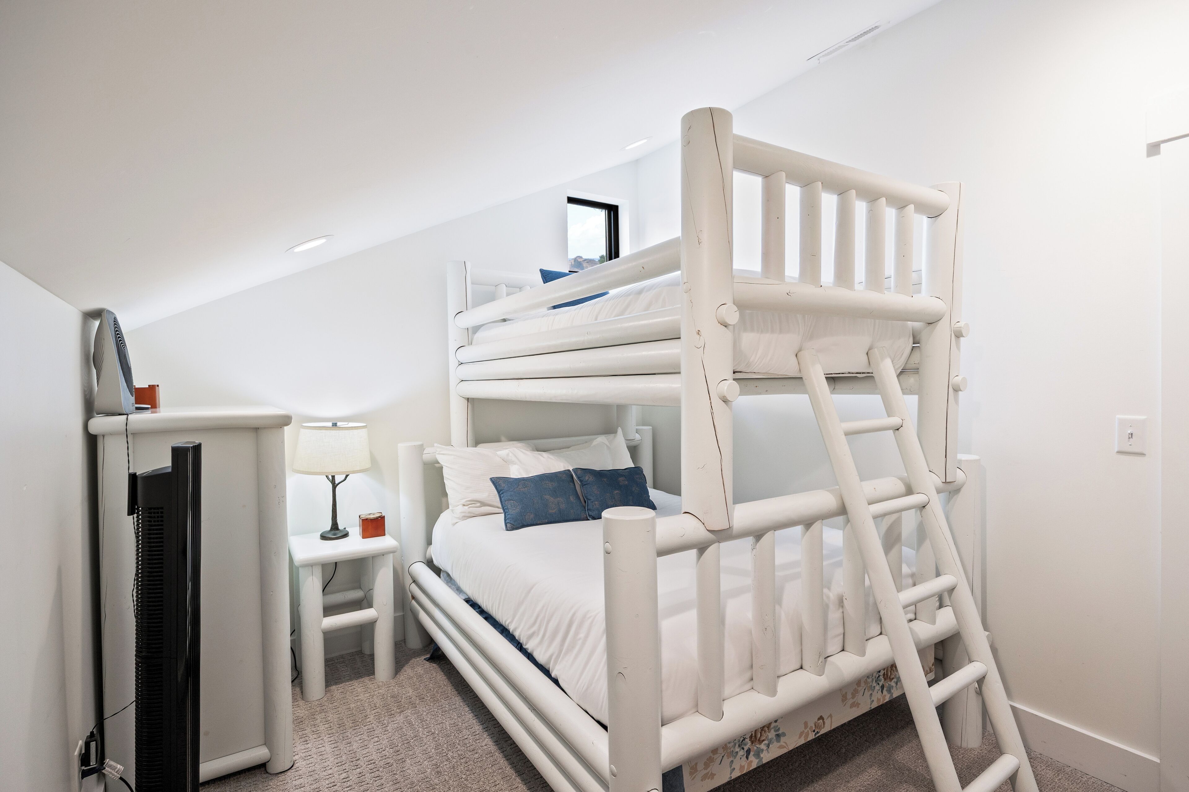 A bunk bed with a ladder, a desk with a lamp, and a television in a room with white walls and carpet.