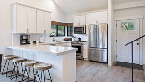 Una cocina moderna con armarios blancos, electrodomésticos de acero inoxidable y una isla central con taburetes de bar.