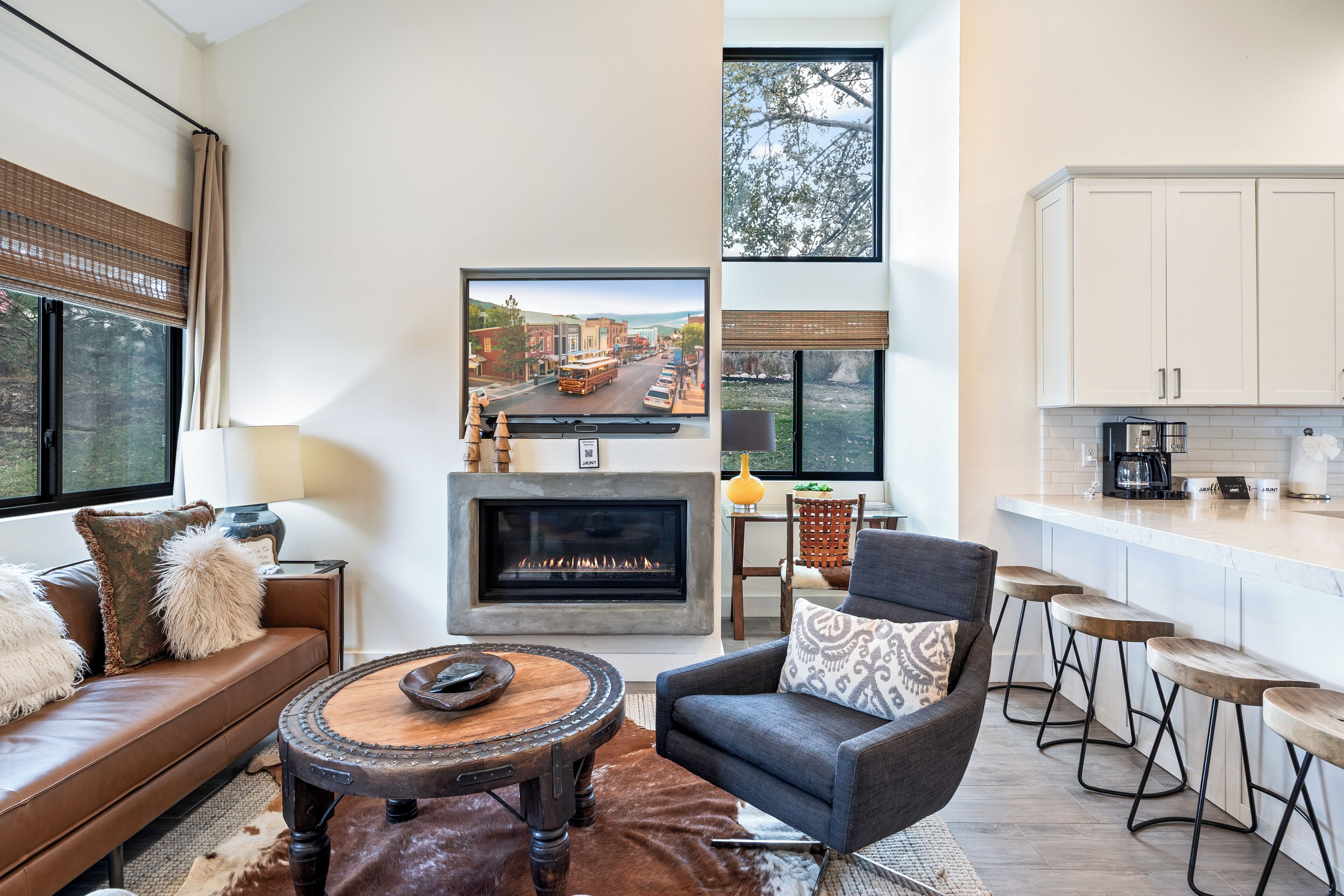 Un salon moderne avec une cheminée, un canapé, une table basse ronde et une vue sur une rue, visible à travers une grande fenêtre.