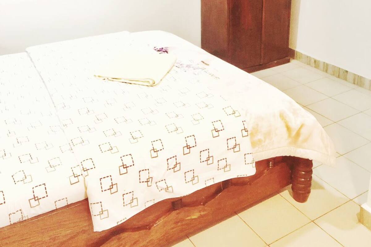 Une chambre à coucher avec un lit en bois, une couvre-lit blanche à motifs et une armoire en bois.