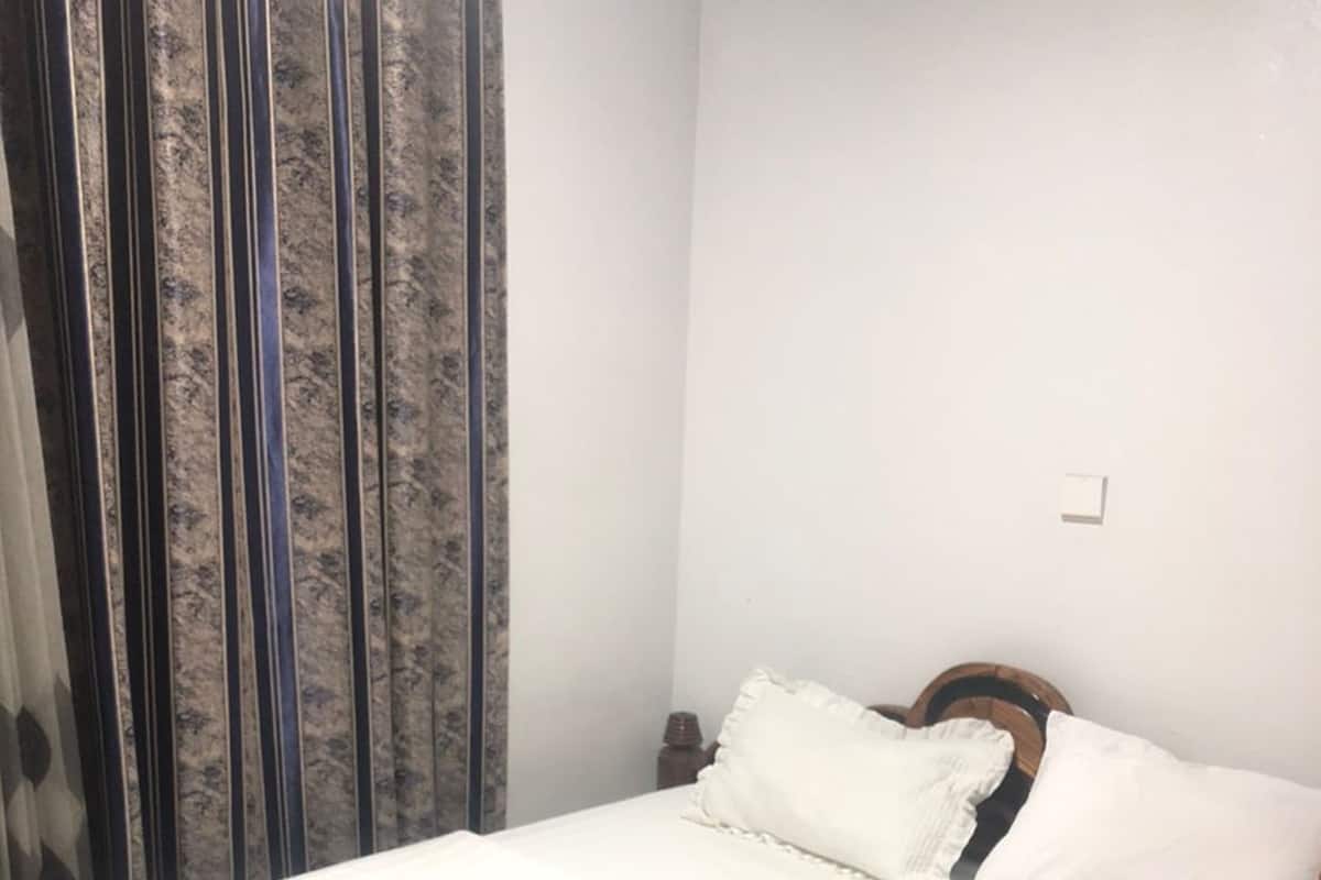 Un lit bien fait, avec une literie et des oreillers blancs, une tête de lit en bois et un rideau à motifs rayés.