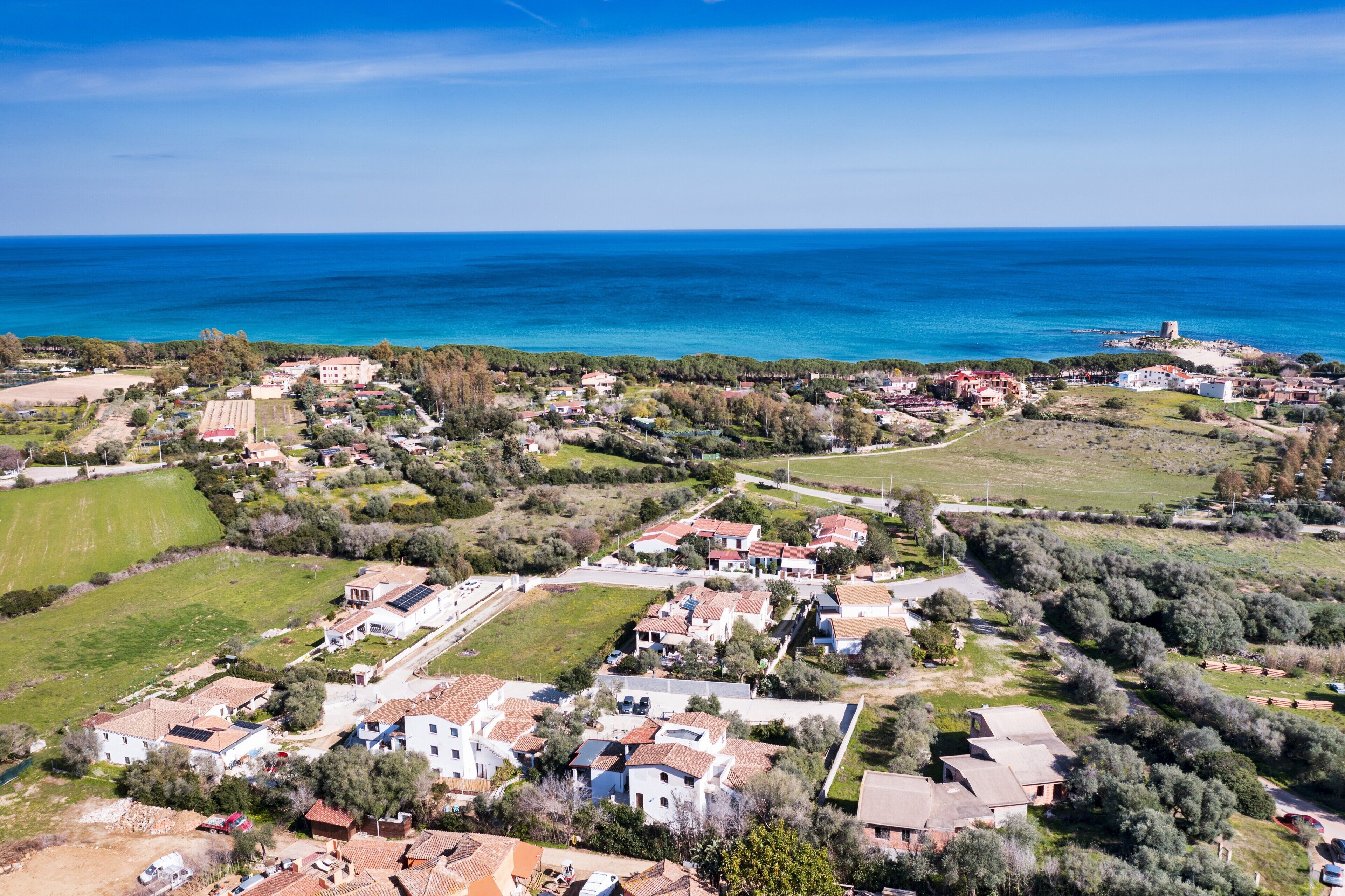 Una cittadina costiera con case, un ampio campo e vista sul mare.