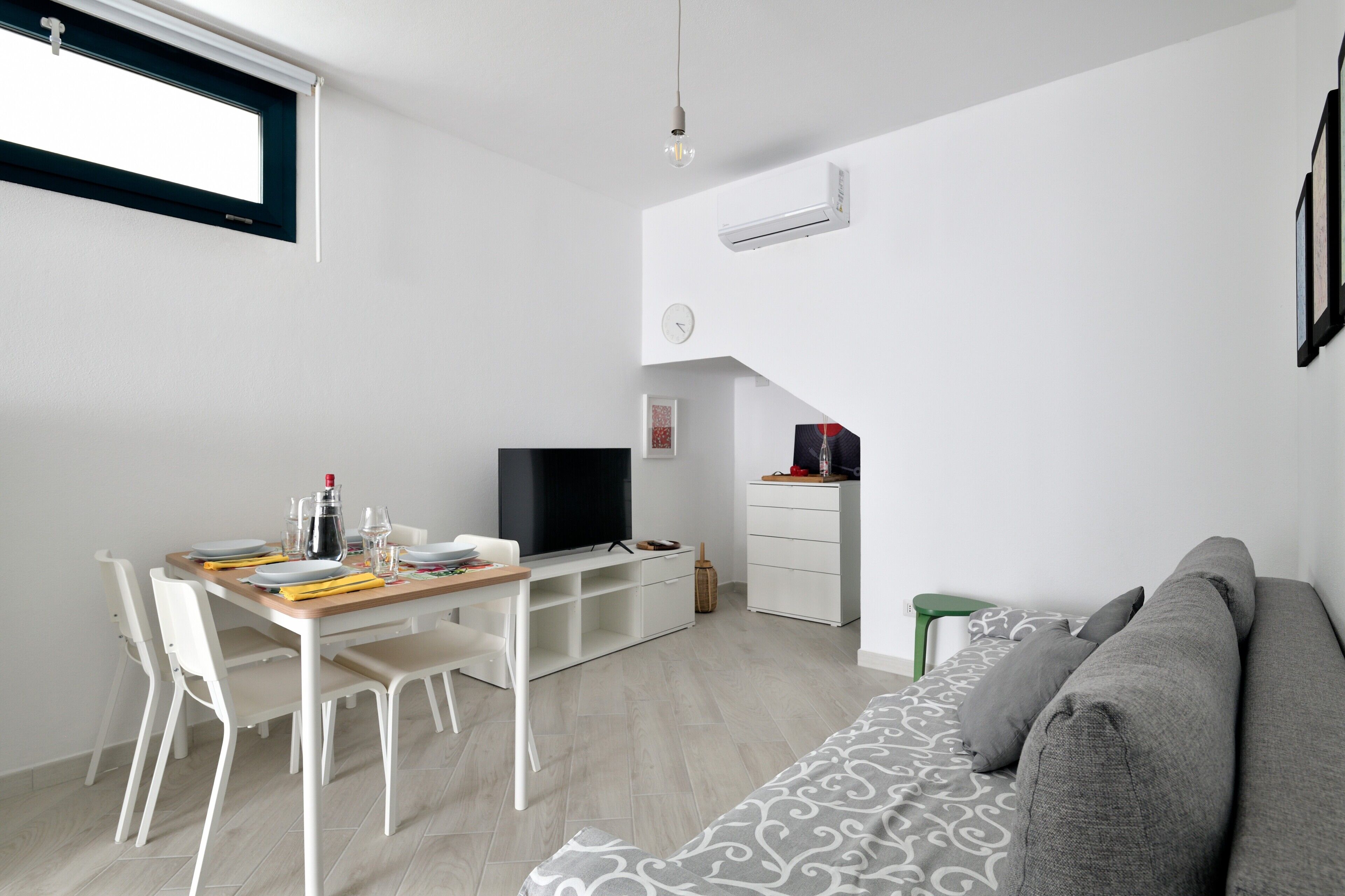 Ein moderner Wohnraum mit Essbereich, Fernseher, Sofa und einer Treppe zu einer oberen Ebene.