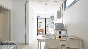 A dining area with a table set for four, a sofa, and a kitchen in the background. - Vacation Home "Appartamentino" with Private Terrace & Wi-Fi (Barisardo)