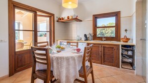 A kitchen with wooden cabinets, a dining table with chairs, a hanging light fixture, and a window with a view.