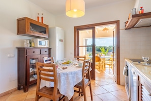 Una cocina con comedor, armarios de madera, un refrigerador y vistas a través de un ventanal.