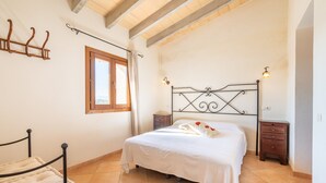A bedroom with a bed, a nightstand, a wooden bench, a window, and a wall-mounted light fixture.
