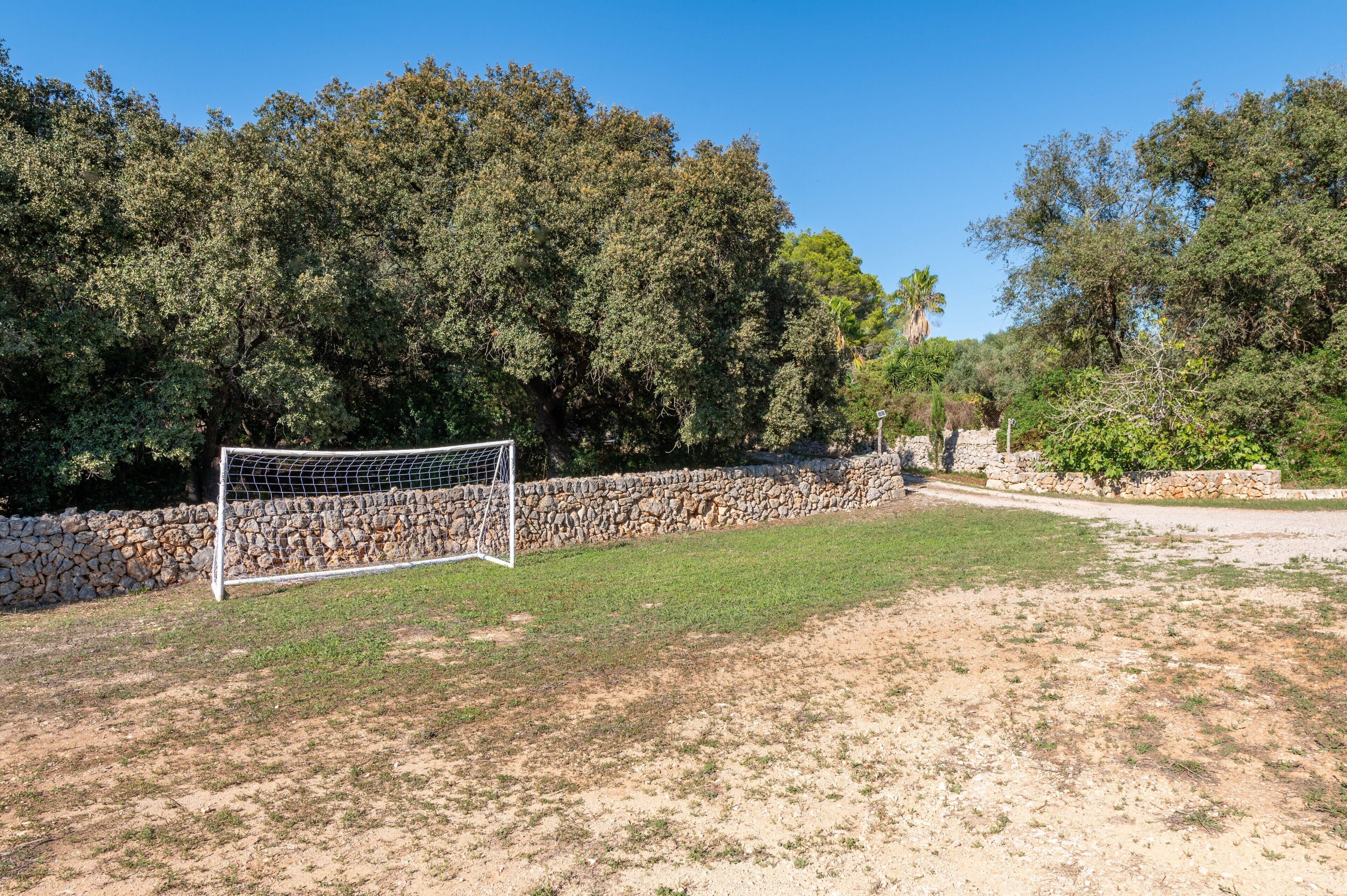 A soccer goal in a grassy area with a stone wall and trees in the background.